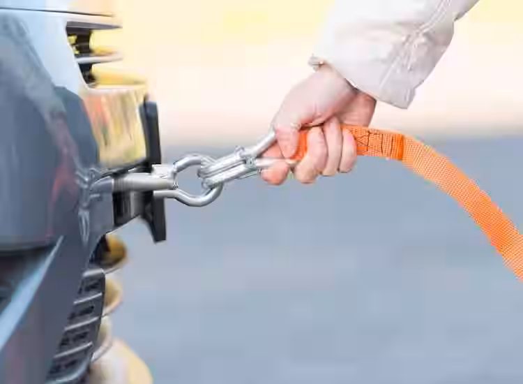 A hand connects an orange tow strap to a gray car.